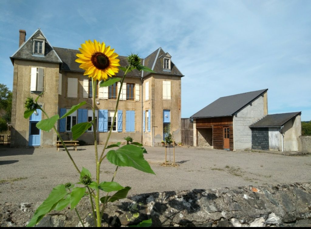 Oude school in Le Puits met op de voorgrond een grote zonnebloem.